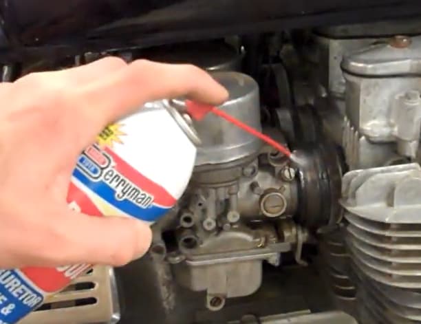 Mechanic performing spray test with aerosol carburetor cleaner on intake boot to detect vacuum leak RPM change