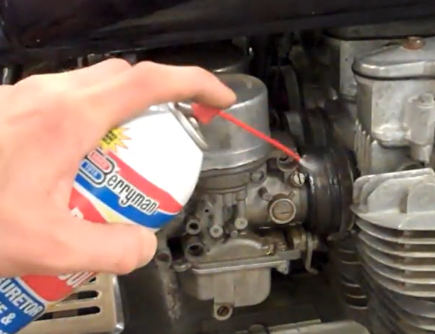 Mechanic performing spray test with aerosol carburetor cleaner on intake boot to detect vacuum leak RPM change