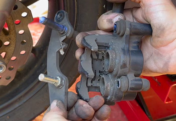 Unbolting the 14mm muffler mounting bolts on the Honda ADV 150 to access the rear caliper