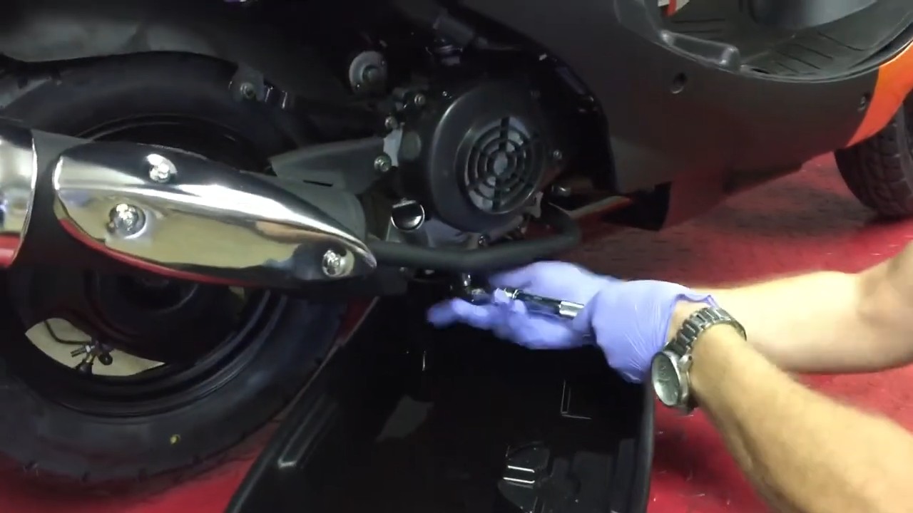 Drain plug removal from warm 139QMB GY6 crankcase showing spring and reusable oil filter assembly