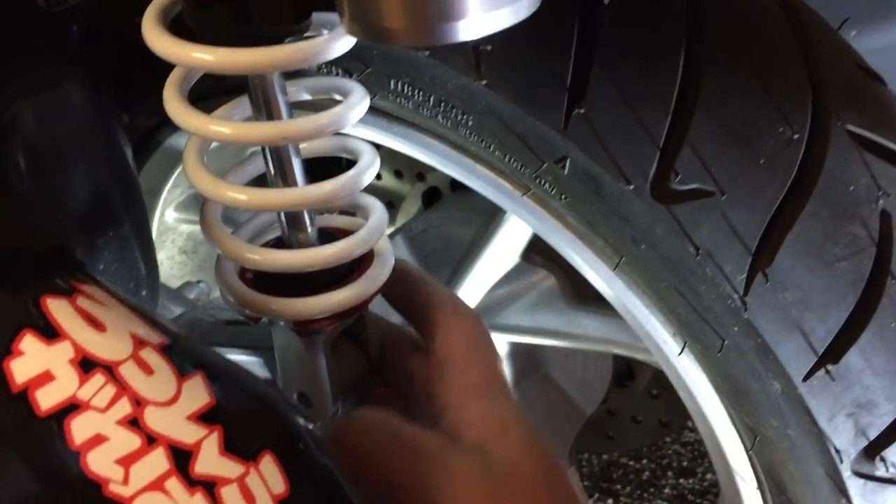 Threading the bottom shock nut from underneath while holding the bolt in position on the left side of the Yamaha NMAX